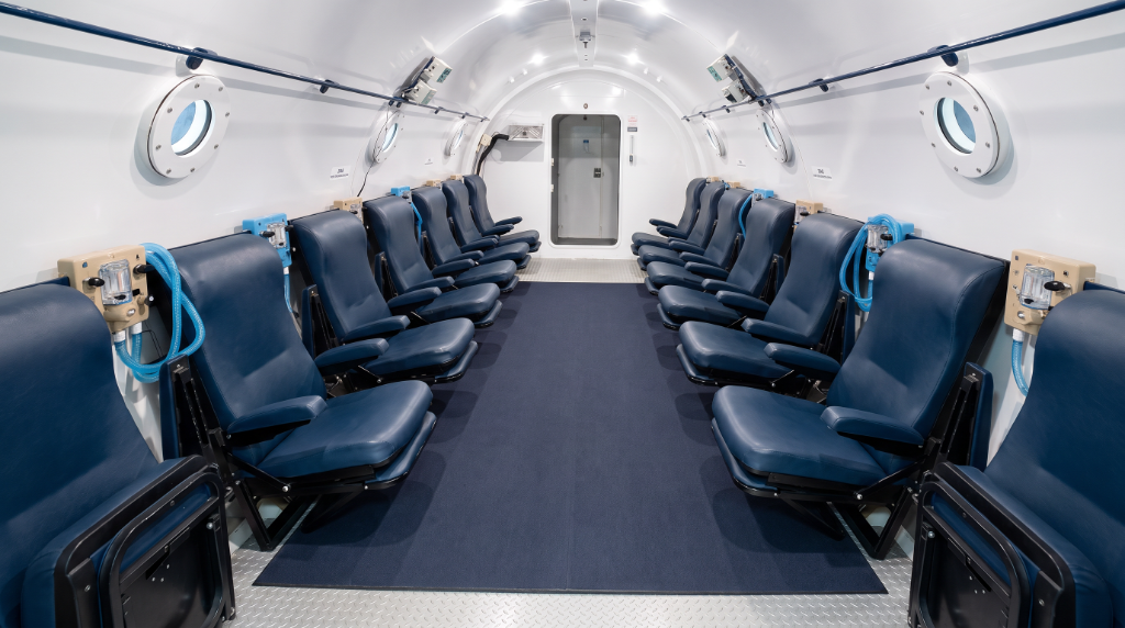 Inside the BRHC 12-person multiplace chamber — two rows of padded seats facing a carpeted aisle